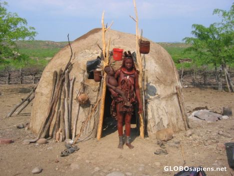 Postcard Himba woman with baby outside hut.