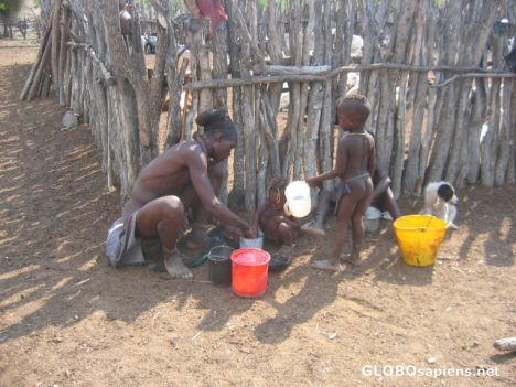 Postcard Himba children helping father make mealie pap