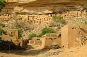 Teli n/ Kani-Kombole; houses & granaries in the front, Pygmy huts clinging to the cliff at the back